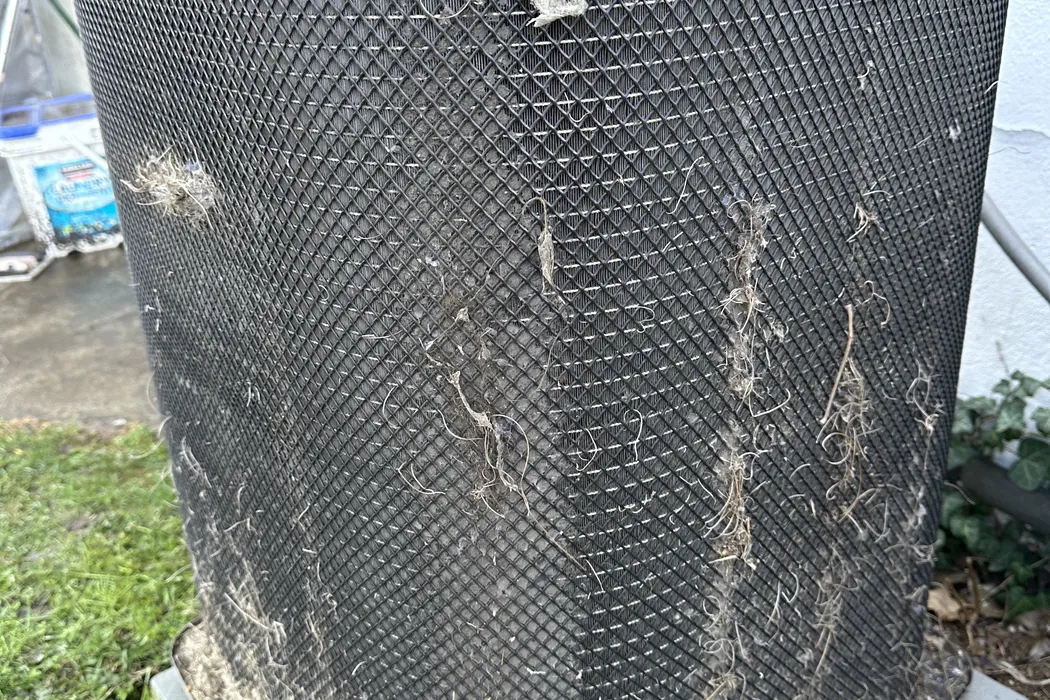 Condenser coil guard clogged with grass and lint before cleaning