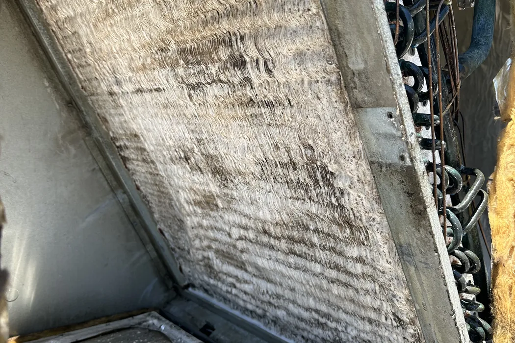Rooftop unit coil dark with dust behind an open panel