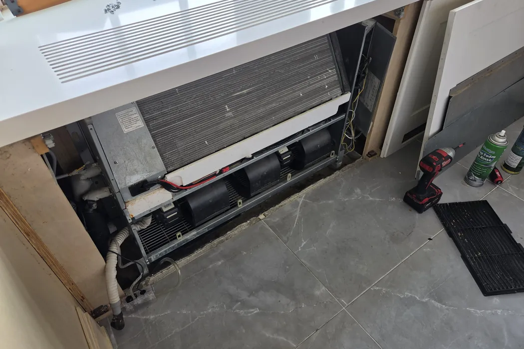 Fan coil blower wheels and coil dark with dust behind an opened panel